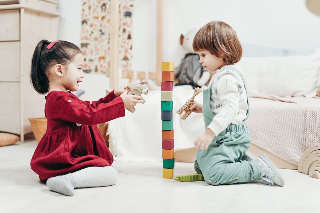 Boy in White Long Sleeve Shirt and Green Pants Sitting on Floor Beside girl in Red